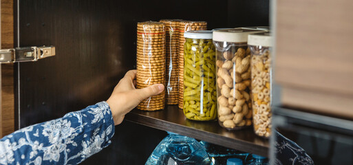 Banner of woman hand checking cookies package to 72 hours survival kit n cupboard. Alert, foresight and self sufficiency strategy. Female preparing emergency food pantry in kitchen for disasters