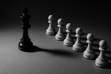 Black king chess piece facing line of white pawn pieces in dramatic shadowed setting, symbolizing strategy and leadership