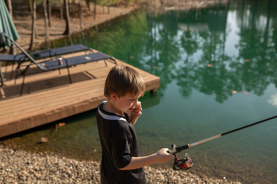 Boy holding a fishing rod near a dock by a green forest pond