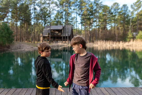 Two brothers talking on a dock by a forest lake with a cabin behind