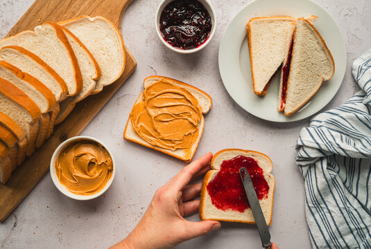Top view peanut and butter jam sandwiches being made on white counter.