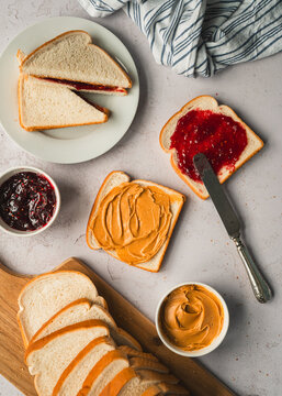 Top view peanut and butter jam sandwiches being made on white counter.