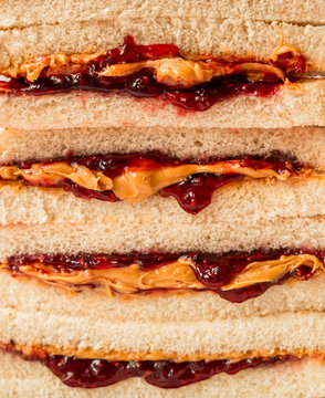 Close up of stack of peanut butter and jam sandwiches on white bread.