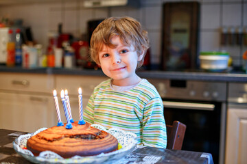 Adorable four year old boy celebrating his birthday and blowing off the candles on the cake,...