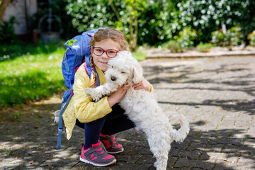 Little girl with her school satchel after school and her cute maltese puppy dog. Happy child and pet. Love.