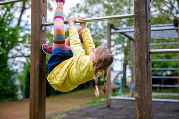 Little girl doing gymnastics on a climbing frame, horizontal bar on school yard. Child enjoying school break.