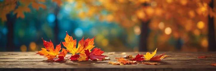  Colorful autumn leaves rest on a wooden table with a blurred forest background, creating a warm scene. © Larysa