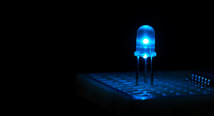 A single, intensely glowing blue LED (Light Emitting Diode) is prominently featured, inserted into a white breadboard against a stark black background