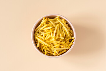 Potatoes Chips. Deep-fried straws of natural potatoes . Top view of an isolated  porcelain bowl with a pile of potato chips on the light orange background . 
