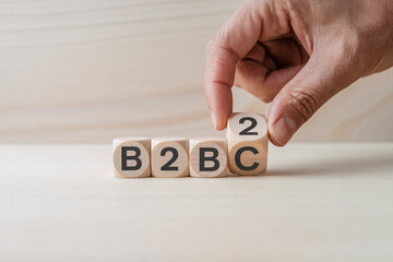 Wooden cubes spelling B2B on light wood table, hand placing last cube, showcasing business-to-business concept