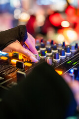 A close-up of a DJ’s hand adjusting knobs and sliders on a vibrant, illuminated audio mixer...