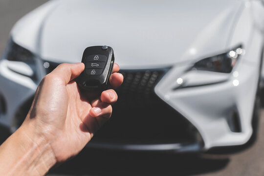 Close-up of a woman unlocking a car using a key fob, with a white car parked in a car park in the background.
