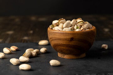 pistachio with salt, fried unpeeled pistachio nuts in a wooden bowl with cracked shell, side view