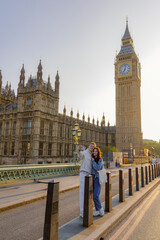 A cheerful and happy couple is joyfully posing for a delightful selfie in front of the iconic Big Ben, capturing the essence of a beautiful, sunny day in the vibrant city of London