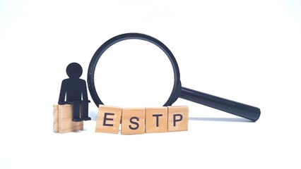 Wooden blocks spelling "ESTP" with a small human figurine toy and a magnifying glass. ESTP is one of the 16 personality types identified by the Myers-Briggs Type Indicator or MBTI.