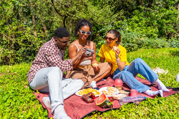 Fototapeta premium Friends taking photos and eating during picnic in a park