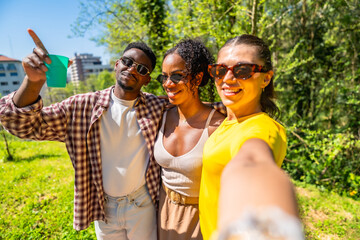 Fototapeta premium Happy friends taking a selfie in the park while pointing finger upward