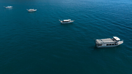 Aerial view of four boats anchored in an arc in the middle of the blue sea.