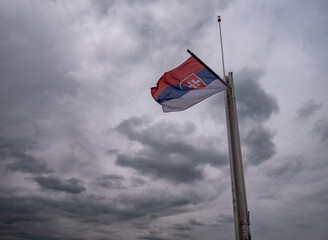 The Slovak national flag flying on a flagpole against a cloudy sky, photographed atop the Spiš Castle tower in Slovakia.