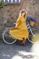 Beautiful happy girl in yellow dress with bicycle in garden in summer