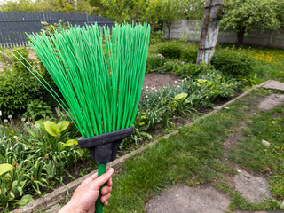 A person holding a green broom in a garden