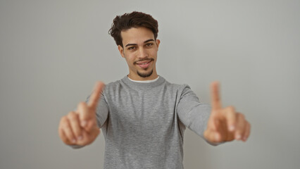 Fototapeta premium Young man with extended fingers smiling confidently against plain white background, embodying a friendly and approachable demeanor