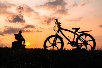 Silhouette of a man with a bicycle on a sunset background.