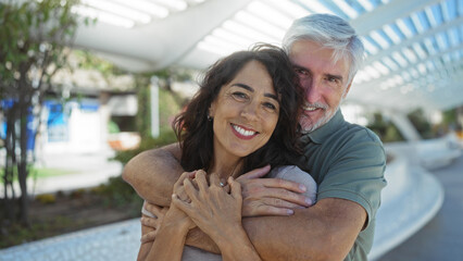 Middle-aged couple embracing outdoors in an urban street setting, showcasing love, happiness, and companionship, while enjoying a sunny day in the city.