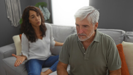 Obraz premium Middle-aged couple in living room having serious discussion reflecting relationship challenges at home.