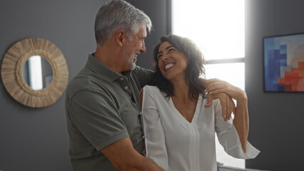 Obraz premium Couple smiling together in their stylish living room, capturing the essence of love and happiness in a modern home setting, with a woman wearing a white blouse and a man embracing her.