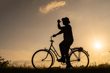 Obraz premium Silhouette of a man in a hat on a bicycle. Sunset background.