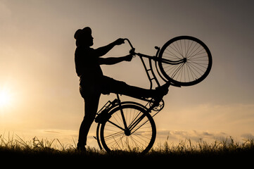 The silhouette of a cyclist stands on the back wheel of a bicycle or bike. Sunset background.