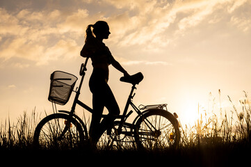 Silhouette of a beautiful unrecognizable girl or woman with a bike. Sunset background.