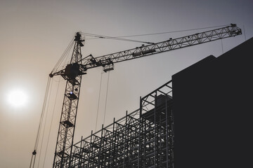 Construction crane silhouette with building and steel structures. Sunset background.