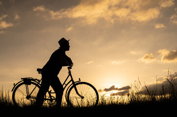 Silhouette of a man on a bike or bicycle and looking forward. Setting sun background.