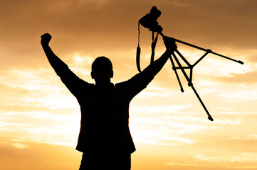 Silhouette of successful photographer with camera on tripod at sunset.