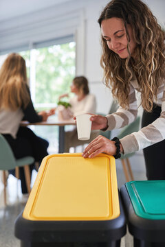 Woman throwing cup in yellow recycling bin in office break room
