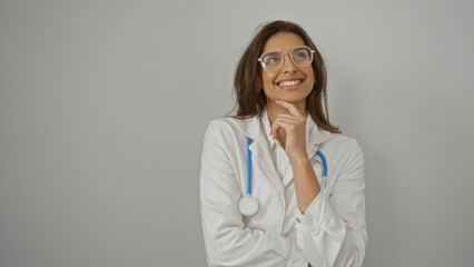 Woman smiling confidently with stethoscope on white background wearing glasses and lab coat looking thoughtful in contemplative pose isolated in professional setting.