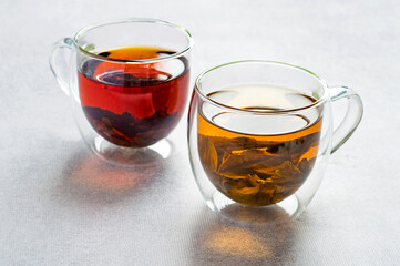 Two cups of assorted black and green tea in transparent double glassware on a light gray background. Horizontal.