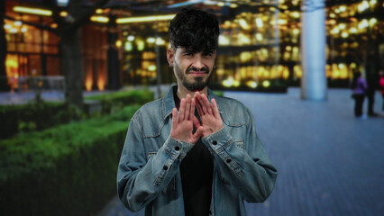 Young man with a disgusted expression standing outdoors on a city street in a denim jacket during...