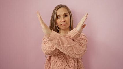 Young woman making stop gesture with hands crossed in front of her against an isolated pink...