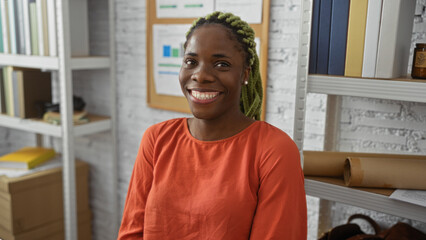 Woman smiling in an indoor office with braided hairstyle, showcasing a welcoming and professional environment with bookshelves in the background.