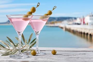 Two pink martinis with olives enjoying seaside view