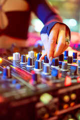 A close-up of a DJ’s hand adjusting the knobs on a vibrant, illuminated sound mixer during a live...