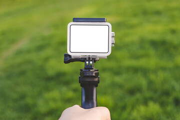 Close-up of the mockup of an action camera in the hand of a guy against a background of green grass.