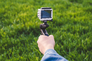 A man shoots on an action camera, holding a tripod in his hand. Against the background of green...