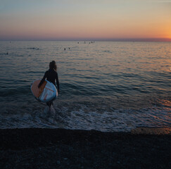 Old aged woman walking with surf board, sunset on sea. Active lifestyle for older senior female