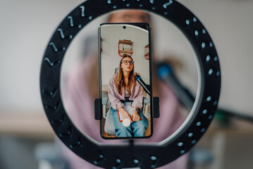Young woman recording a podcast using a ring light and a smartphone