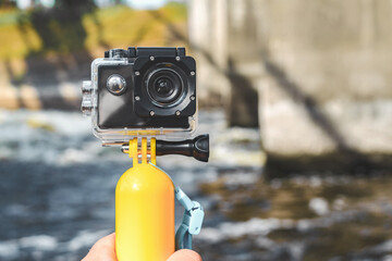 Action camera close-up, waterproof body and yellow float. Water bokeh background with large streams of water with waves.