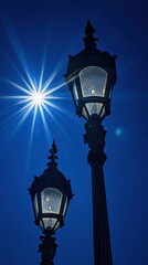 Two Victorian street lamps stand silhouetted against a deep blue sky with bright sunburst overhead low angle shot